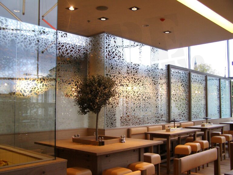 Restoranisaal, kus klaasist vaheseinad on kaetud mattklaasikilega lehemustriga, eraldades lauad ja andes ruumile hubase privaatsuse, klaasseinte kiletamine