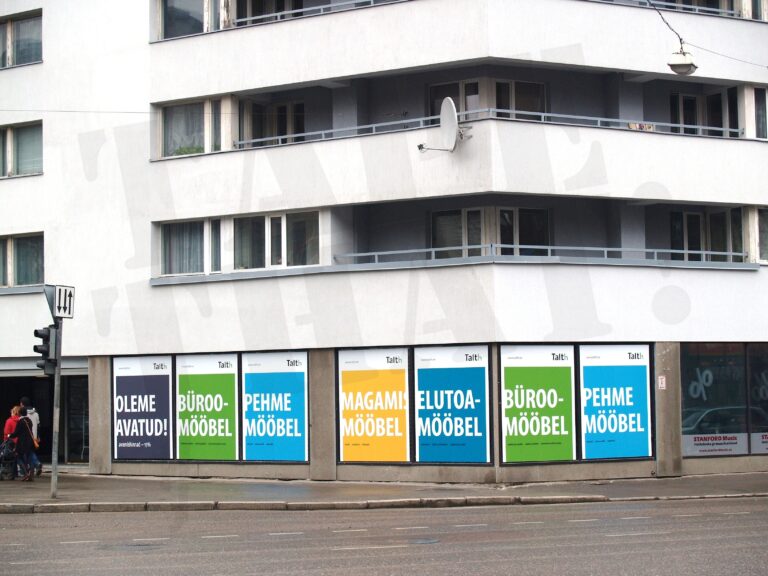 Talth mööblipoe esimese korruse vaateaknad kiletatud suurte värviliste aknakleebistega tekstidega nagu „büroomööbel“ ja „pehme mööbel“