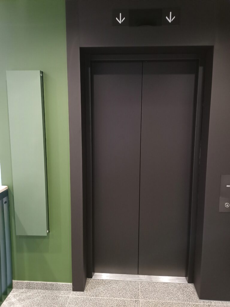 Musta dekoratiivkilega kaetud liftiuksed ja piidad, mis on sobitatud rohelise-musta sisekujundusega