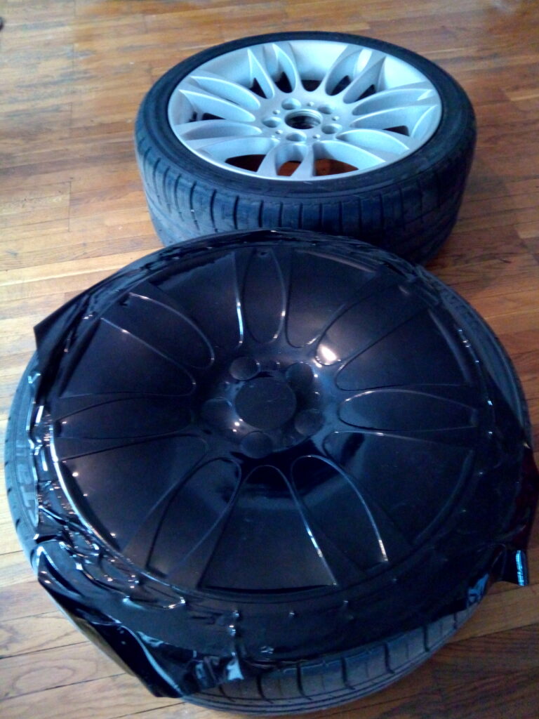 Hõbedane valuvelg ja selle kõrval gloss musta kilega kaetud velg, velgede kiletamine